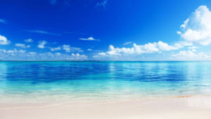 Acqua blu chiaro con onde leggere e cielo sereno pieno di nuvole bianche.