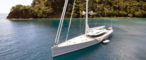 Yacht a vela bianca ancorato in acque calme con alberi sullo sfondo.